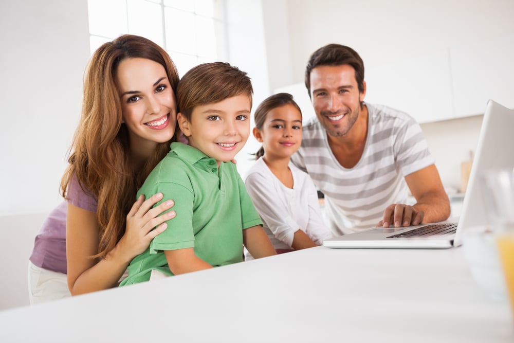 Happy family looking at the camera with a laptop in kitchen